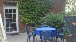 Eine Terrasse mit rundem Tisch und vier Stühlen, einem Blumentopf und einer Backsteinmauer mit Grünpflanzen.