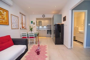 Een moderne woonkamer met een bank, een eettafel met stoelen, een keuken met kasten en apparatuur, en een gang naar een badkamer.
