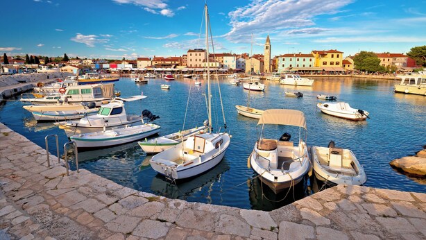 A marina with various boats docked, a stone quay, and buildings in the background. - Holiday apartment with one bedroom and balcony with sea view (Fažana)