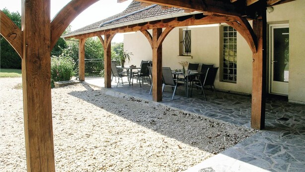 A covered patio with stone flooring and wooden beams, featuring outdoor seating and a view of a garden. - Stunning home in Eyliac (Eyliac)