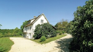 A white two-story house with a sloped roof, a small balcony, and a chimney. There is a gravel driveway leading to the house, surrounded by lush greenery and trees. - Stunning home in Eyliac (Eyliac)