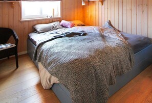 A wooden-paneled room with a bed, a chair, and a window. - Vacation cottage Bogense, Germany (Quern)