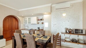 Un comedor con puerta de madera, una cocina con armarios blancos y un estante empotrado para microondas.