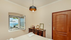 Un dormitorio con una cama, un aparador de madera, un espejo, un reloj y una ventana con un persiano abierto.