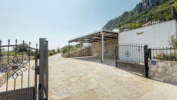 A stone-paved entrance to a building with a metal gate, a covered outdoor area, and a mountainous backdrop.