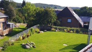 Un jardin à l’arrière d’une maison, avec une pelouse, une terrasse en bois, une maison en briques et des panneaux solaires sur le toit.