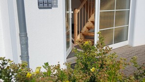 Une maison à l’extérieur blanc, avec un escalier en bois et une porte-fenêtre coulissante donnant sur un intérieur également en bois.