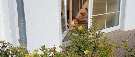 A house with a white exterior, a wooden staircase, and a sliding glass door leading to a wooden interior.