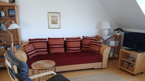 Un salon confortable avec un canapé, un fauteuil, une lampe, un téléviseur et une bibliothèque.