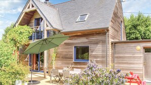 A two-story wooden house with a sloped roof, a satellite dish, and a patio with outdoor furniture. - Nice home in Plounéour-Trez with sauna (Plounéour-Trez)