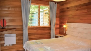 A wooden room with a bed, a window with curtains, a wall-mounted heater, and a bedside lamp. - Nice home in Plounéour-Trez with sauna (Plounéour-Trez)