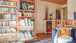 A cozy living room with a bookshelf filled with books, a small cabinet with more books, a blue sofa with a white throw, and a wooden ceiling. - Nice home in Plounéour-Trez with sauna (Plounéour-Trez)