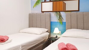 Een hotelkamer met twee bedden, een nachtkastje met een lamp, en een wanddecoratie van een strandgezicht.