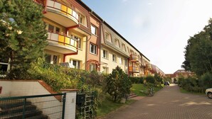 Una hilera de edificios residenciales de varios pisos con balcones, un camino pavimentado y abundante vegetación.