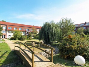 Un ponte di legno sopra un sentiero sterrato che conduce a un edificio con tetti in tegole rosse e balconi.