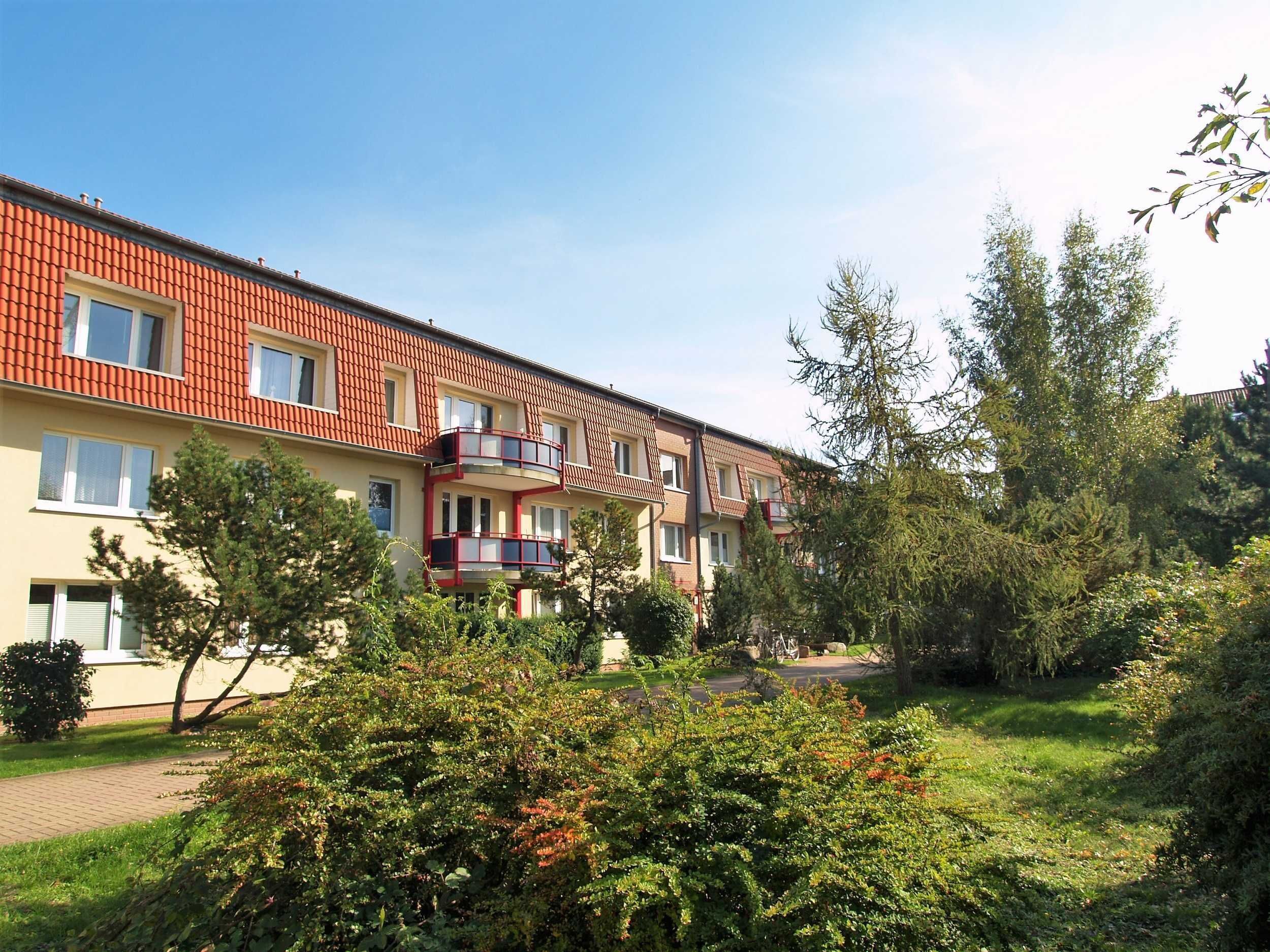 A multi-story residential building with a red-tiled roof, balconies, and a well-maintained garden area.