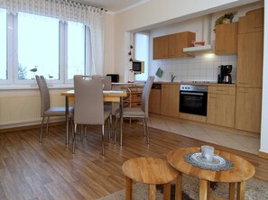 Une cuisine moderne avec des meubles en bois, un coin repas comprenant une table et des chaises, et une fenêtre avec des rideaux.