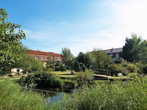 Ein friedlicher Hotelinnenhof mit Teich, üppigem Grün und zwei Gebäuden mit roten Dächern.