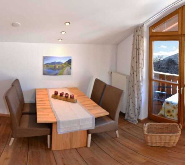 Un coin repas avec une table en bois, des chaises rembourrées, un chemin de table blanc et un tableau représentant un paysage.