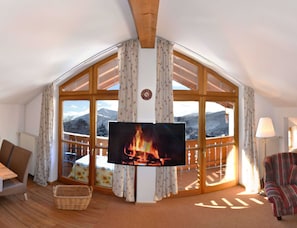Un salon chaleureux avec une grande télévision, des poutres en bois, un canapé et une vue sur les montagnes.