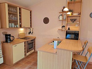 Una cucina compatta con mobili in legno, forno a incasso, macchina per il caffè e un piccolo angolo ristoro con una sedia.