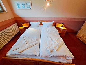 A double bed with white linens and towels, wooden headboards, bedside lamps, and a radiator.