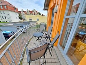 A balcony with outdoor seating, a view of the city, and a building with orange walls.