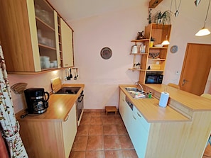 Une cuisine compacte avec des meubles en bois, un four encastré, une machine à café et un évier.