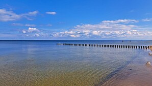 Una playa tranquila con agua cristalina, un muelle de madera y un barco a lo lejos.