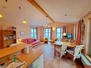 A cozy living room with a wooden sofa, a dining table with chairs, a television, and a bookshelf.