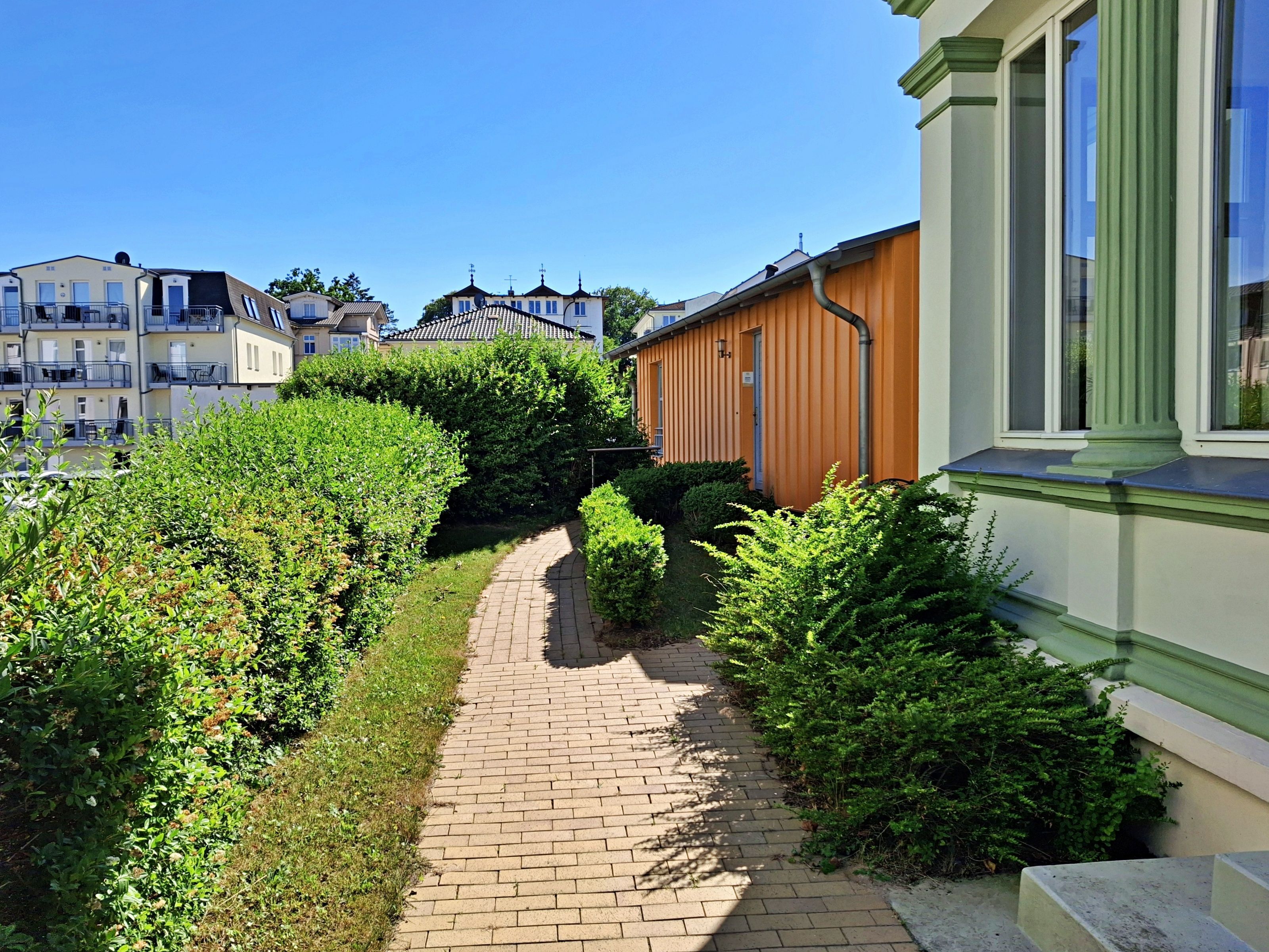 A pathway leading to a row of residential buildings with a green hedge on one side.
