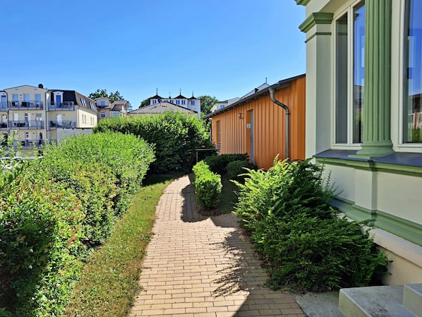 Ein Weg führt an einer Reihe von Wohngebäuden vorbei, begleitet von einer grünen Hecke.