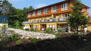 Ett hotell med flera våningar, en gul fasad, balkonger med utomhusmöbler och en stenmur som stödjer marken i förgrunden.