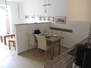 Uma sala de jantar com uma mesa de madeira, quatro cadeiras, uma máquina de café e quadros nas paredes.