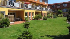 Ett hotell i två våningar med en gul fasad, en uteservering och en välskött trädgård.