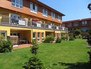 Un hotel de dos pisos con fachada amarilla, zona de estar al aire libre y un jardín cuidado.