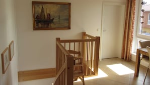 En trappa med träräcken som leder upp till en liten plattform, en målning av ett segelfartyg på väggen, en dörr och ett fönster med gardiner.