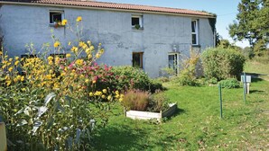 Un edificio de dos plantas con antena parabólica, varias ventanas y un jardín con flores amarillas y arbustos.