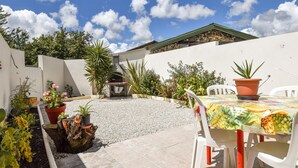 Un patio con una parrilla, plantas en macetas y una mesa con sillas.