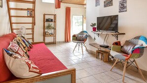 Una sala de estar con un sofá rojo, una escalera de madera, un televisor sobre un mueble de madera y una estantería.