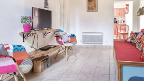 Una sala de estar con televisión, estantería, sofá rojo y cocina a la vista.