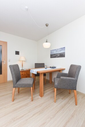 Un coin repas avec une table en bois, deux chaises grises, une lampe et un tableau au mur.