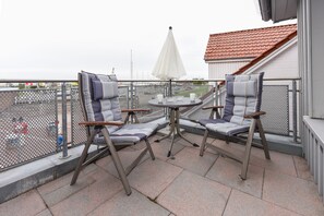 A balcony with two chairs and a small table, a white umbrella, and a view of a building with a red roof.