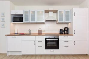 A modern kitchen with white cabinets, a microwave, an oven, and a coffee maker. - Luv - House harbor view (Esens)