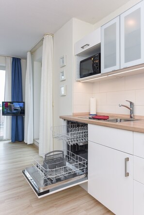 Une cuisine moderne équipée d’un lave-vaisselle, d’un four à micro-ondes et d’un téléviseur fixé au mur.