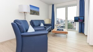 Ett modernt vardagsrum med två blå soffor, ett soffbord i trä, en golvlampa och en tv-skärm.