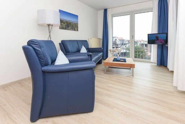 A modern living room with two blue sofas, a wooden coffee table, a floor lamp, and a TV screen.