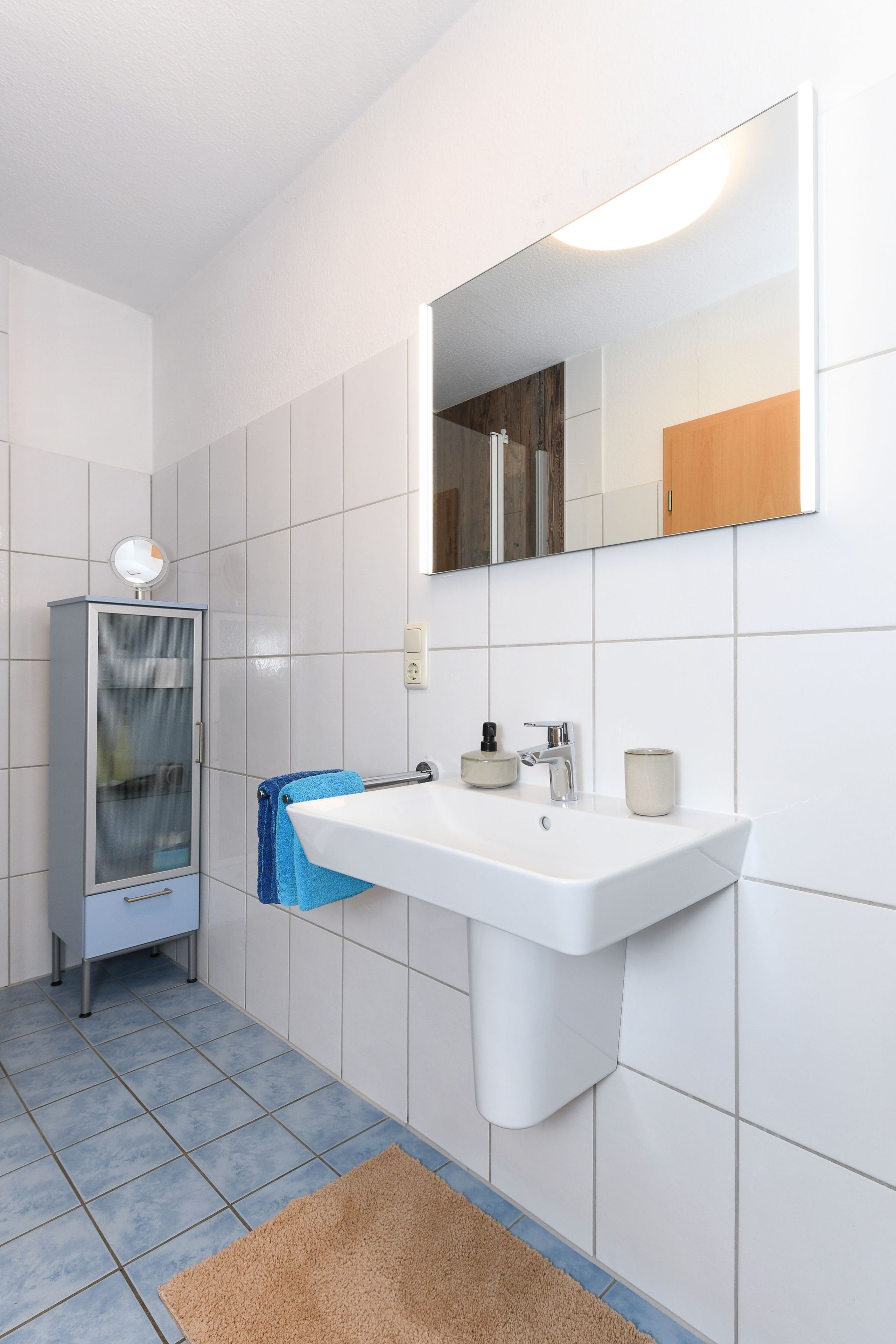 Casa de banho com lavatório branco, espelho, armário e toalha azul.