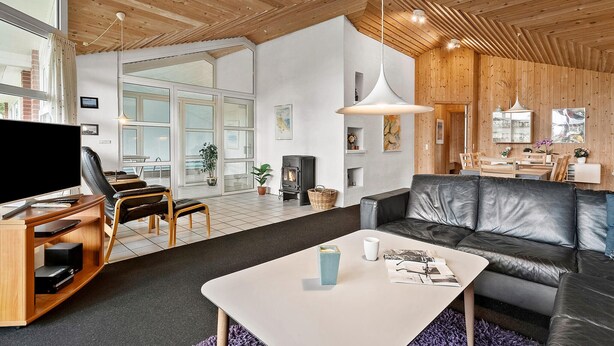A modern living room with a fireplace, leather sofa, and a dining area. - Amazing home in Blåvand with sauna (Blåvand)
