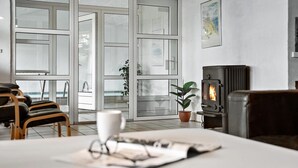 A modern living room with a fireplace, large windows, and a view of the outside. - Amazing home in Blåvand with sauna (Blåvand)
